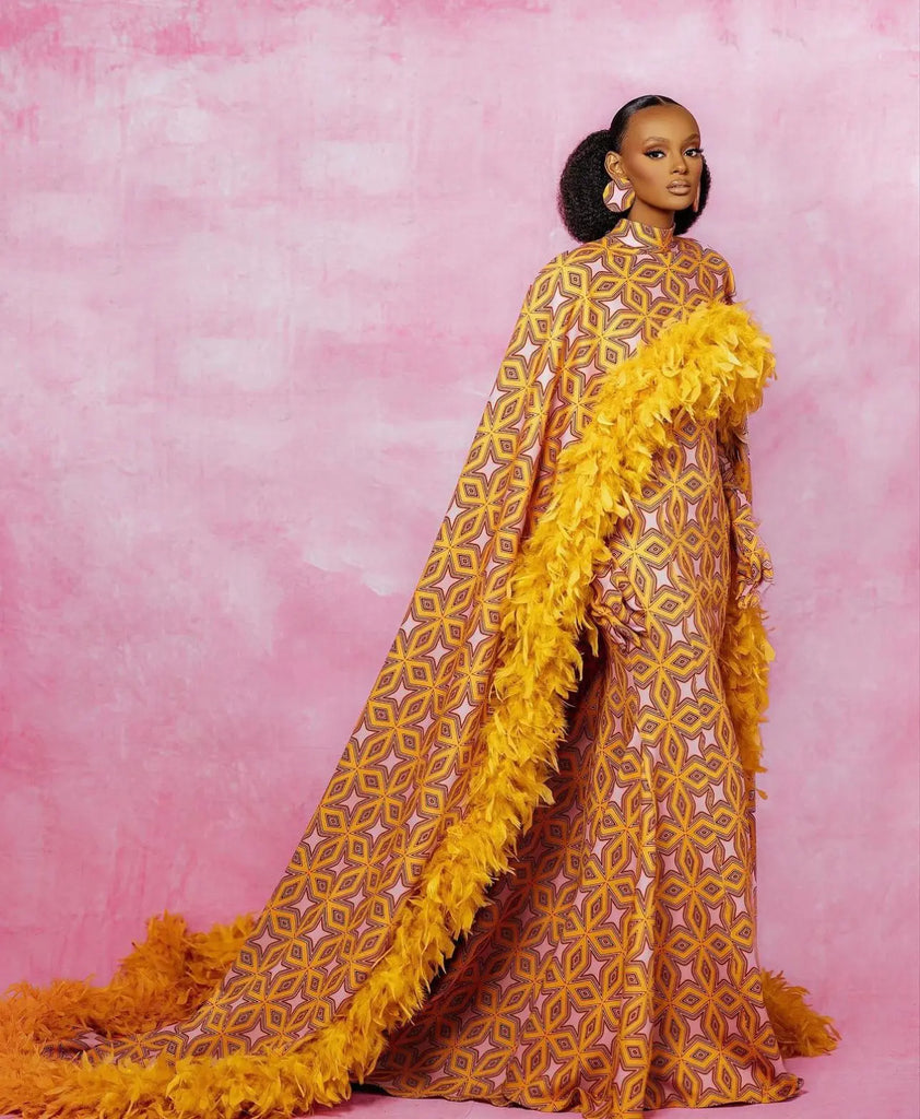 Vibrant African-inspired long dress with intricate yellow and maroon floral pattern, complemented by a dramatic feathered yellow shawl, showcasing bold and fashionable design.