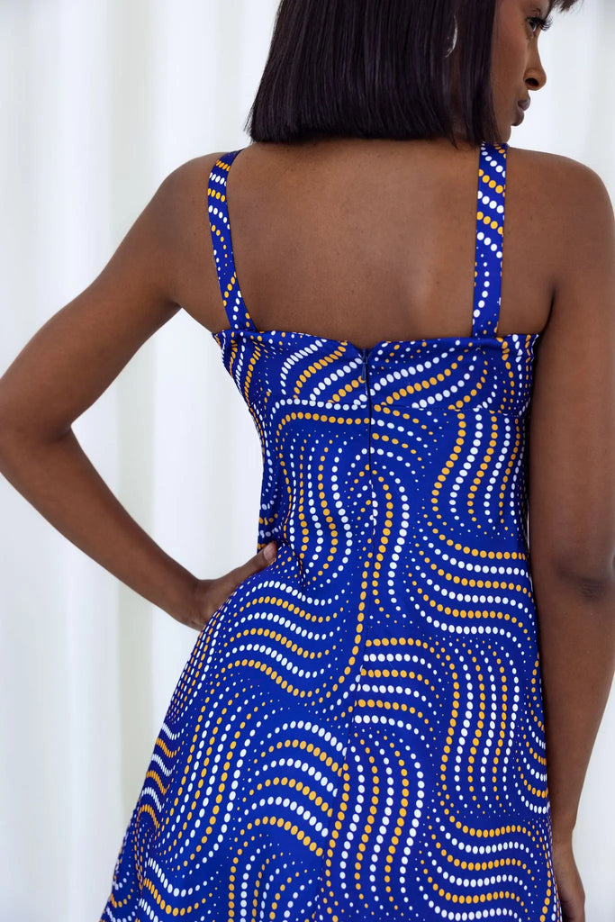 Vibrant African print dress with bold, swirling pattern in shades of blue and yellow. Sleeveless design with thin straps and fitted bodice. Showcases elegant, contemporary African fashion.