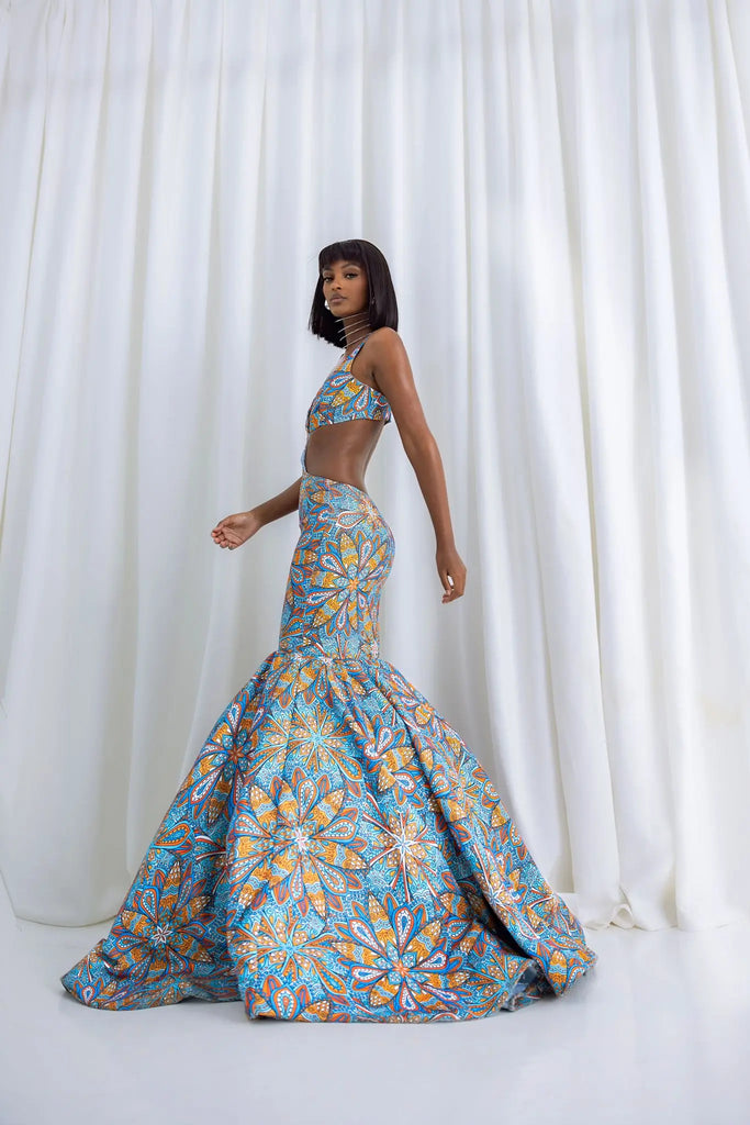 Vibrant African-inspired mermaid gown with intricate floral pattern, sleeveless crop top design, and bold color palette, styled against a plain white backdrop.