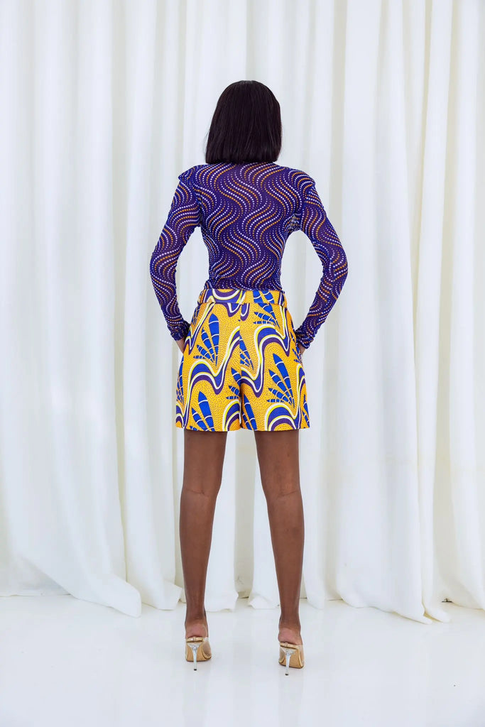 Vibrant African print shorts by Claude Kameni featuring a bold, eye-catching pattern in shades of purple and yellow.