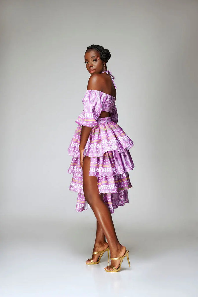 Beautiful purple off-the-shoulder dress with tiered ruffles, worn by a stylish African model on a plain white background.